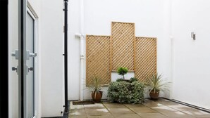 Un patio limpio y con baldosas, una pared blanca, una valla de madera celosía y plantas en macetas.