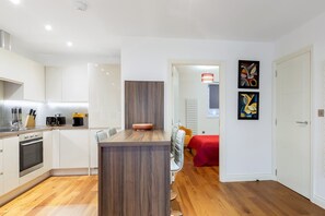 A modern kitchen with white cabinets, a wooden island, and a dining area with a red tablecloth. - Modern and Large Oasis Flat in Camden With Patio (London)