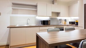 Una cocina moderna con armarios blancos, una encimera de madera y una zona de comedor con una mesa y sillas de madera.
