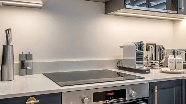 A modern kitchen with grey cabinets, a built-in oven, a coffee machine, and a sink. - Modern Spacious Studio in Chelsea by King s Road (London)