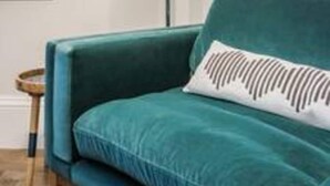 A teal sofa with a patterned pillow, a floor lamp, and a wooden floor. - Modern Spacious Studio in Chelsea by King s Road (London)