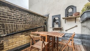 A wooden table and chairs set on a balcony with a brick wall and a metal railing. - Unbeatable Location in Camden-spacious Studio Flat (London)