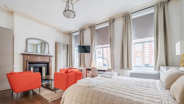 A hotel room with a large bed, a fireplace, a desk with a chair, and a TV. - Unbeatable Location in Camden-spacious Studio Flat (London)