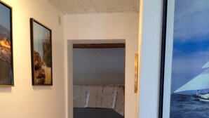 Ein schmales Gang mit einem Bett in der Ecke, einem gerahmten Bild links und einem gerahmten Bild rechts.