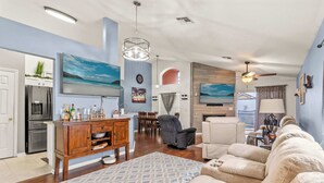 Een ruime woonkamer met een grote beige bank, een houten entertainmentsysteem en een eethoek met uitzicht op de oceaan.