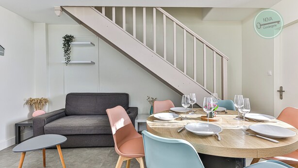 A dining area with a round table, chairs, and a staircase. - La Maison du Soleil Sion sur l'océan (Saint-Hilaire-de-Riez)