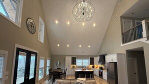 Uma sala de estar ampla com um sofá grande, um candelabro e uma cozinha ao fundo.