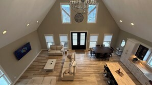 Um loft espaçoso com pé direito alto, um lustre, área de jantar e cozinha.