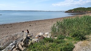 En kustnära strand med ett stenigt landskap, en klar himmel och en stadssiluett i fjärran.