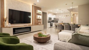 Uma sala de estar moderna com uma televisão de tela grande, uma mesa de centro de madeira e sofás verdes.