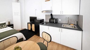 A compact hotel room with a kitchenette, a bed with green bedding, a small dining table, and a chair. - Studio Paris 18eme Montmartre, 2 personnes (Paris)