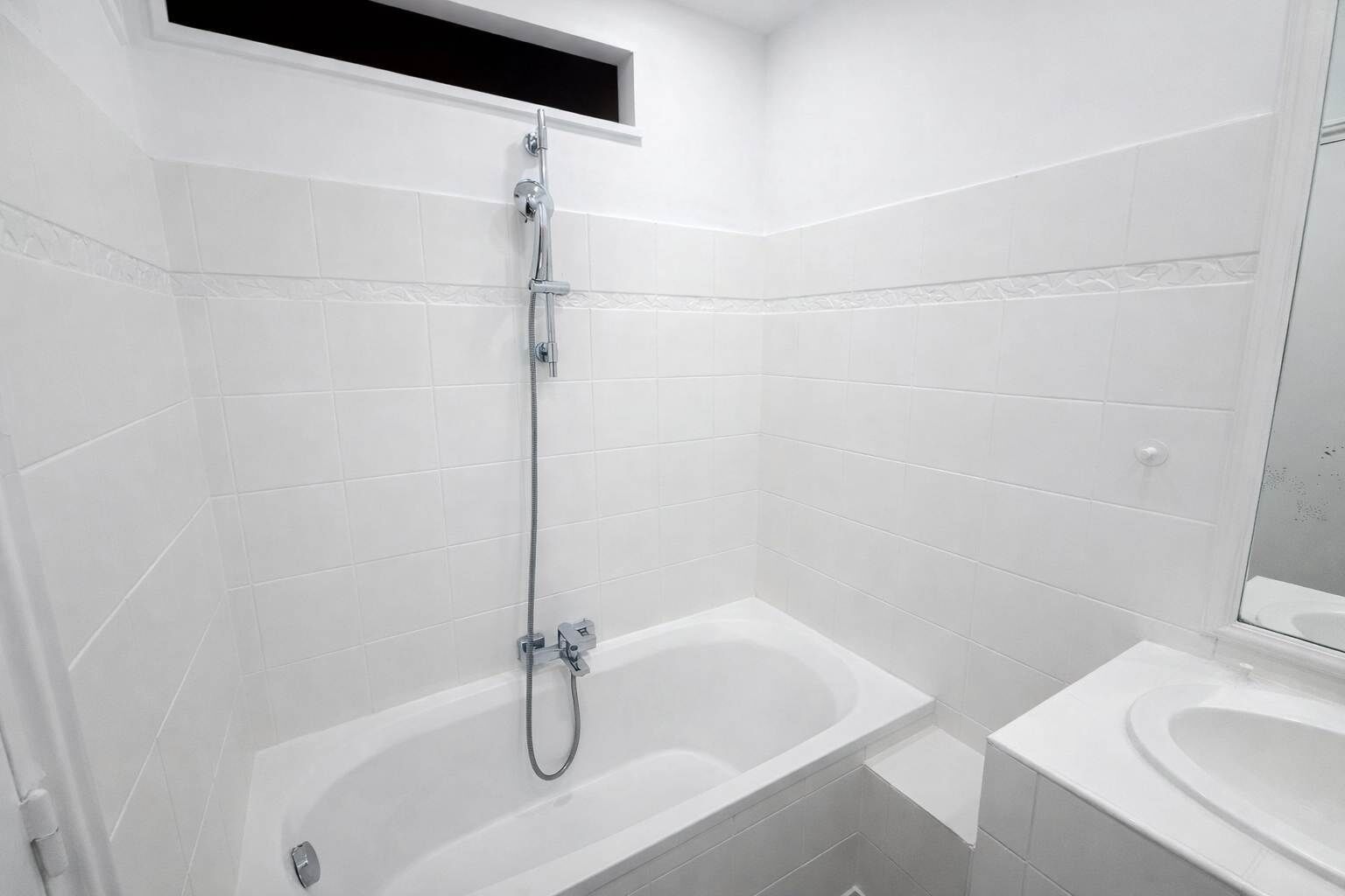 Un baño moderno con azulejos blancos, ducha con cabezal de ducha manual y bañera separada.