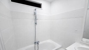 A modern bathroom with white tiles, a shower with a handheld showerhead, and a separate bathtub. - Studio Paris 18eme Montmartre, 2 personnes (Paris)