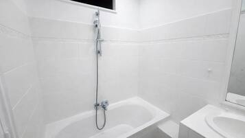 Un baño moderno con azulejos blancos, ducha con cabezal de ducha manual y bañera separada.