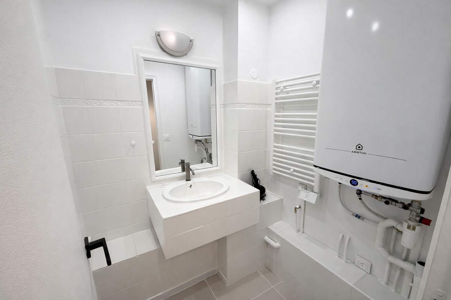 Un baño moderno con un lavabo blanco, espejo y paredes cubiertas de azulejos blancos.