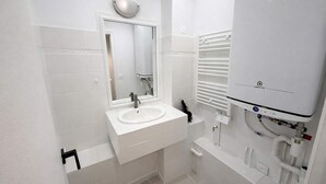 A modern bathroom with a white sink, mirror, and white tiled walls. - Studio Paris 18eme Montmartre, 2 personnes (Paris)