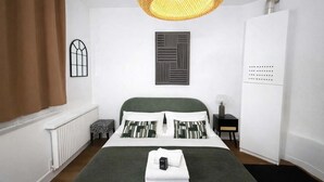 A neatly arranged bedroom with a bed, a radiator, a window with curtains, a wall-mounted artwork, a bedside table with a lamp, and a wardrobe. - Studio Paris 18eme Montmartre, 2 personnes (Paris)
