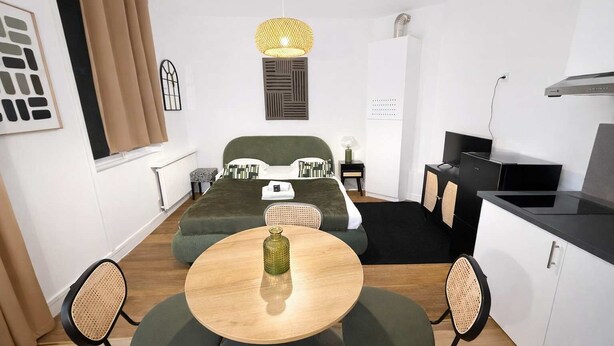A compact hotel room with a bed, a dining table with chairs, a kitchenette, and a hanging light fixture. - Studio Paris 18eme Montmartre, 2 personnes (Paris)