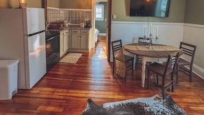 Une cuisine chaleureuse avec un plancher en bois, un lustre, une table à manger avec des chaises et un téléviseur fixé au mur.