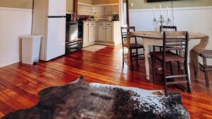 Une cuisine spacieuse avec un plancher en bois, un lustre, un coin repas avec une table et des chaises en bois, et un téléviseur fixé au mur.