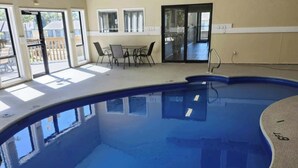 Una piscina interior con vistas despejadas del entorno, que incluyen una mesa y sillas, y ventanas amplias que dejan entrar luz natural.