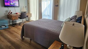 Un dormitorio con cama, escritorio, silla, televisor, ventilador de techo y cortinas.