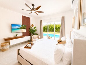 Ein modernes Schlafzimmer mit einem großen Bett, einem Deckenventilator, einem Fernseher und Blick auf einen Swimmingpool.