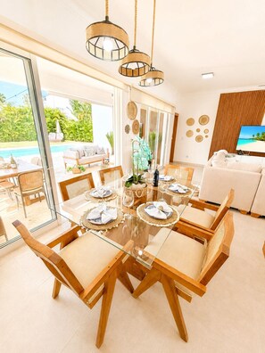 Un coin repas avec une table en verre, des chaises en bois et une vue sur une piscine à l’extérieur.