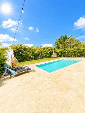 Ein Swimmingpool mit Liegestuhl und Sonnenschirm, umgeben von Grün und blauem Himmel.
