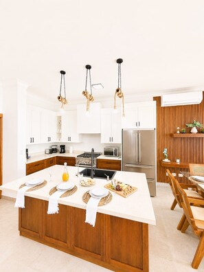 A modern kitchen with white cabinetry, a central island, and a dining area with wooden chairs. - 3bd with rooftop ocean view in Sosua Ocean Village (Sosúa)