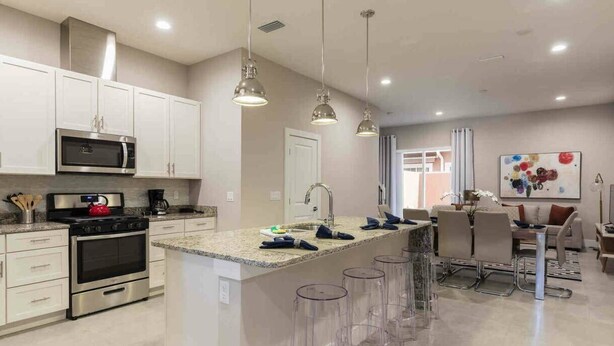 A modern kitchen with white cabinets, stainless steel appliances, and a central island with bar stools. - 4BR Townhome 15min to Disney (Kissimmee)