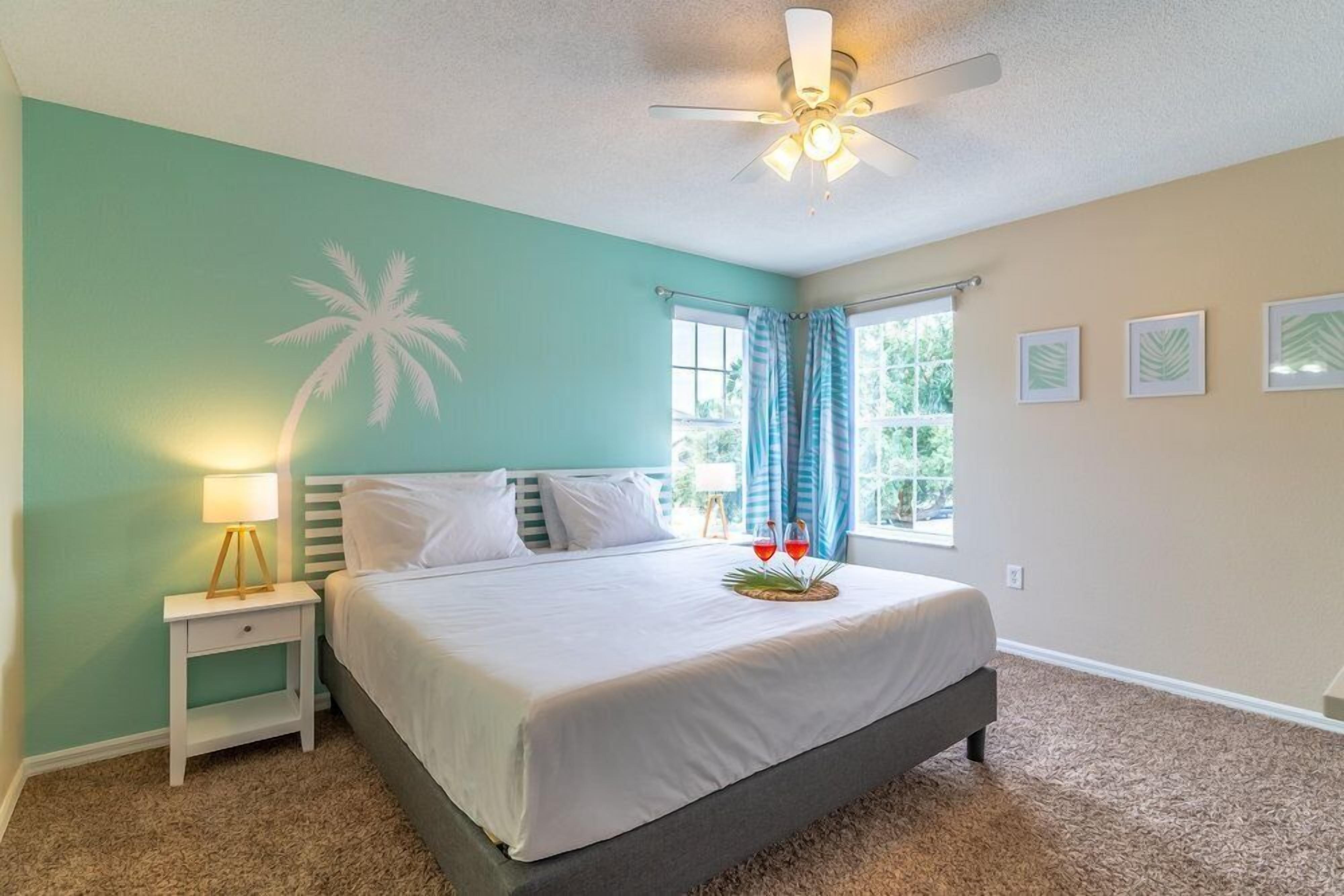 A bedroom with a bed, a nightstand, a ceiling fan, a window with curtains, and framed pictures on the wall.