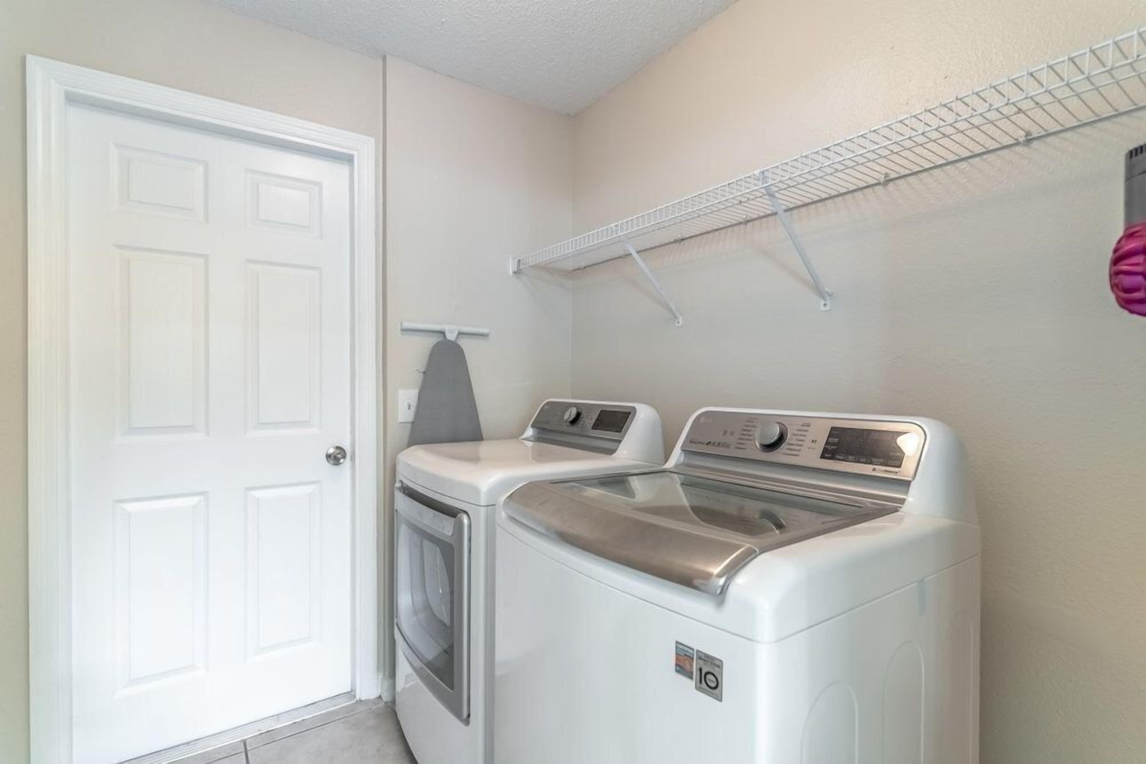 Une buanderie équipée de deux machines à laver et deux sèche-linge superposés, une porte blanche et une étagère en métal au-dessus des sèche-linge.