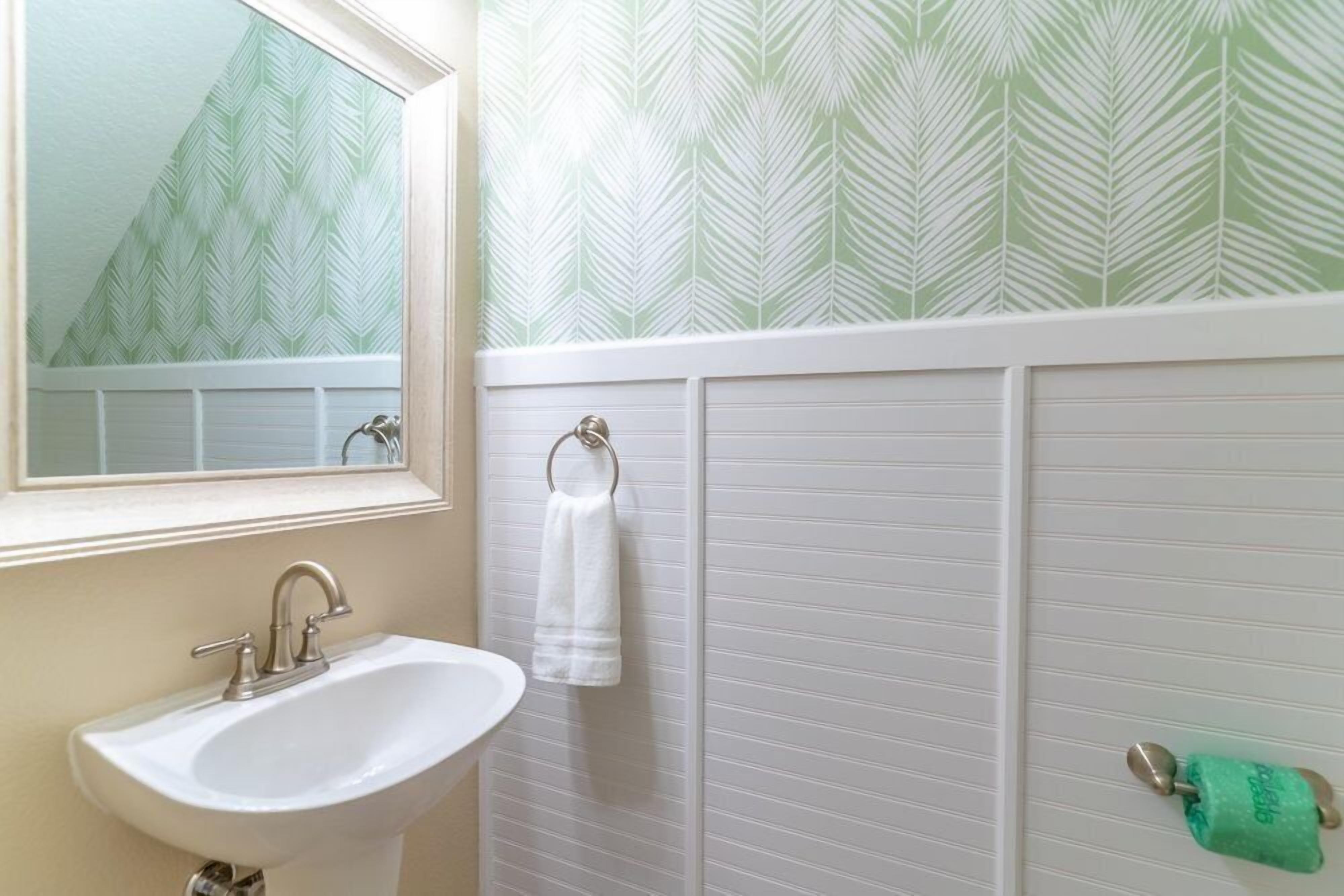 A bathroom with a white sink, a mirror, a towel rack, and a toilet paper holder.