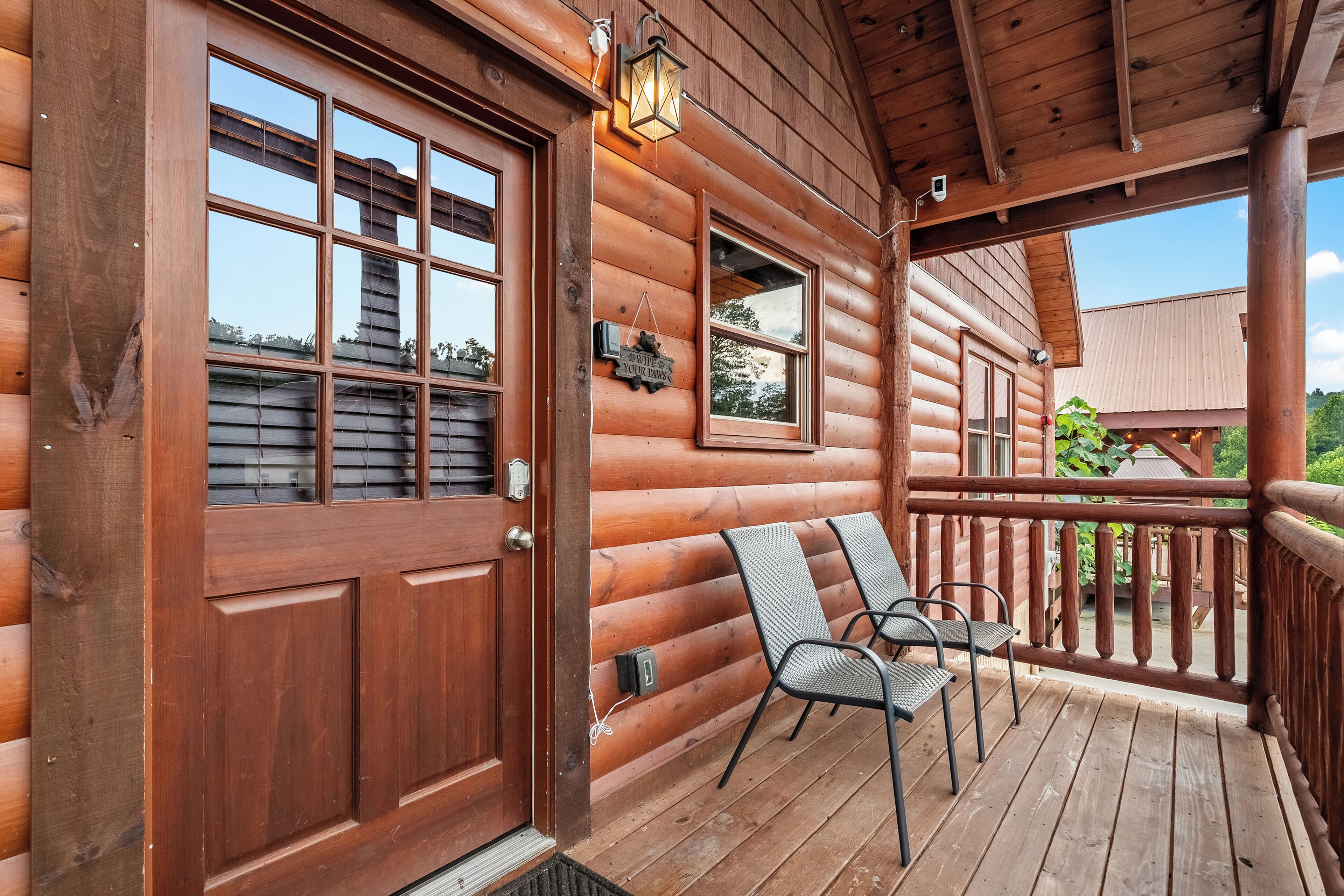Une cabane en bois avec une véranda, deux chaises et une pancarte indiquant « Bienvenue ».