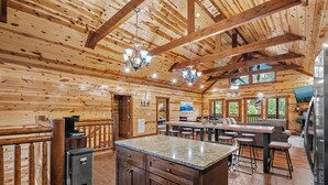 A spacious wooden cabin interior with a kitchen area, dining space, and a bar. - Private Indoor Heated Pool, Arcade, HotTub Sleeps24 (Sevierville)