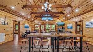 A spacious wooden cabin with a large dining table, bar stools, and a ceiling fan. - Private Indoor Heated Pool, Arcade, HotTub Sleeps24 (Sevierville)
