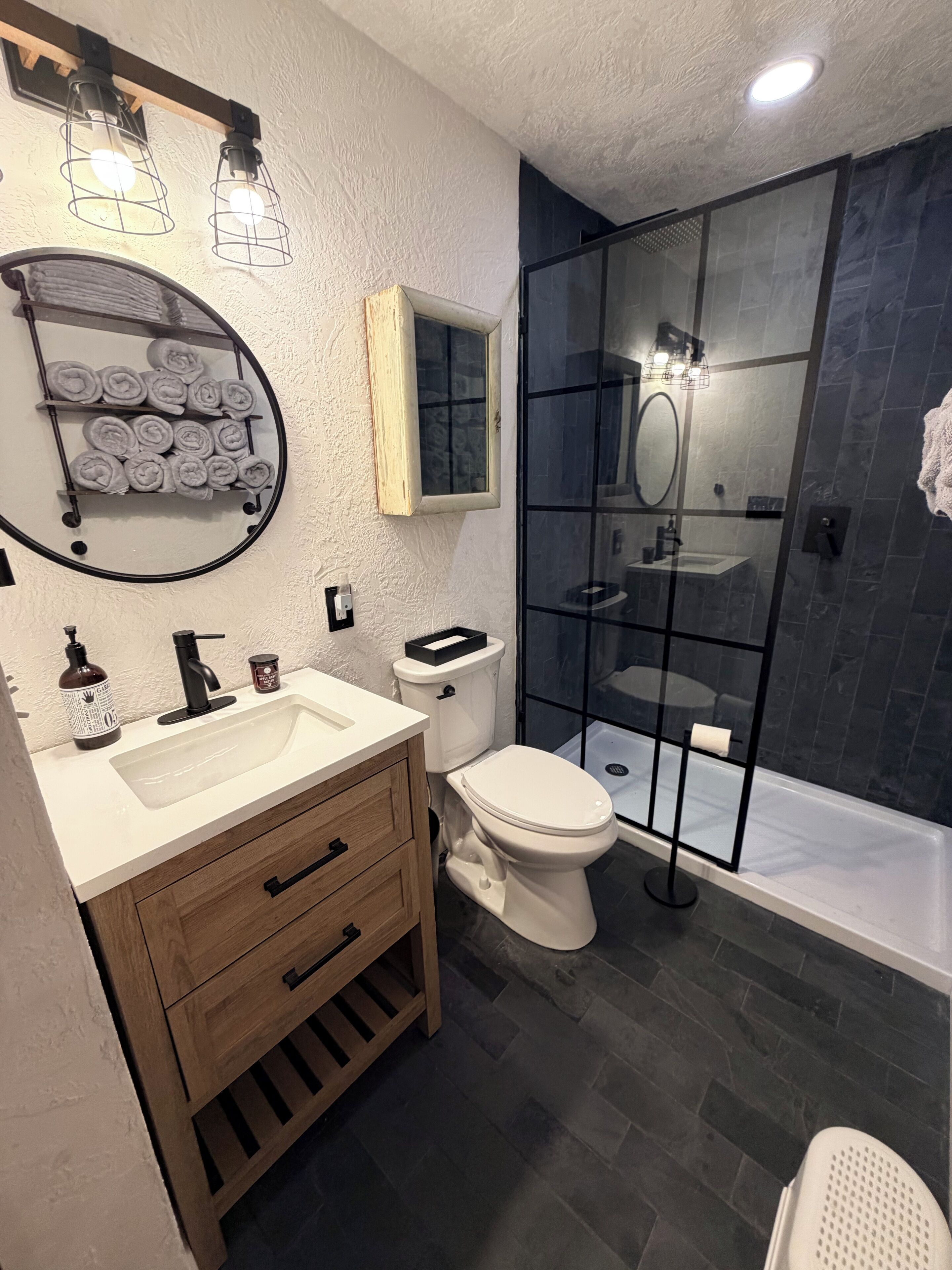 A modern bathroom with a white sink, wooden vanity, a toilet, and a glass-enclosed shower area.