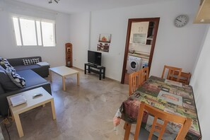 Ein Wohnzimmer mit einer Couch, einem Fernseher, einem kleinen Tisch und einem Essbereich mit Stühlen.