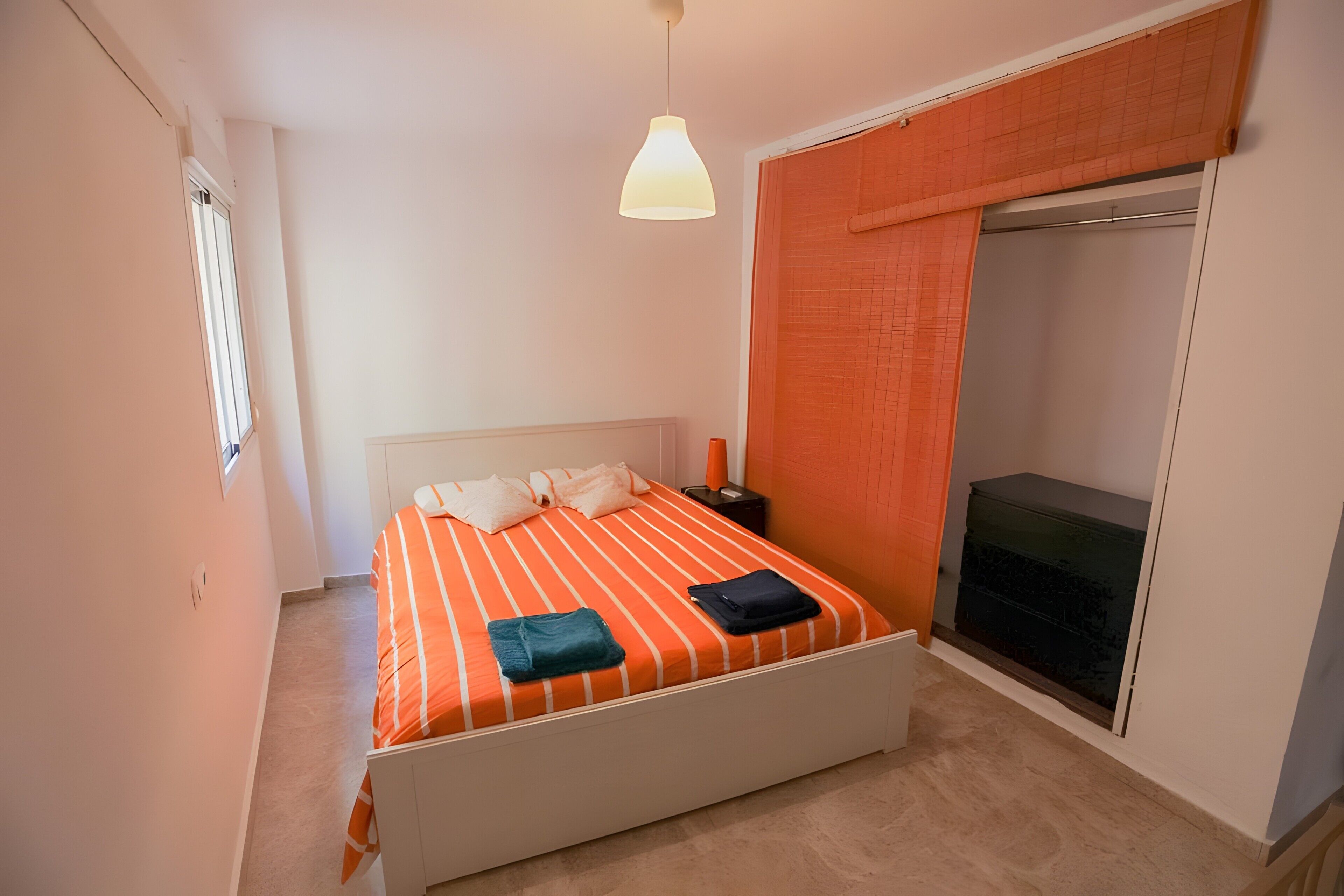 Un dormitorio con cama, mesita de noche, armario y lámpara colgante.