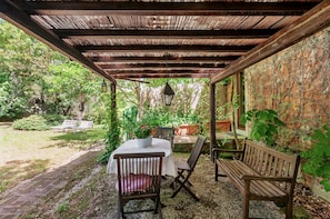 A covered patio with a table and chairs, surrounded by greenery and a brick wall. - Orcio – Romantic studio with private terrace near the pool (Reggello)