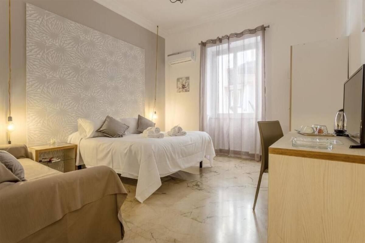 Habitació d'hotel amb llit, escriptori, cadira, televisió i finestra amb cortines.
