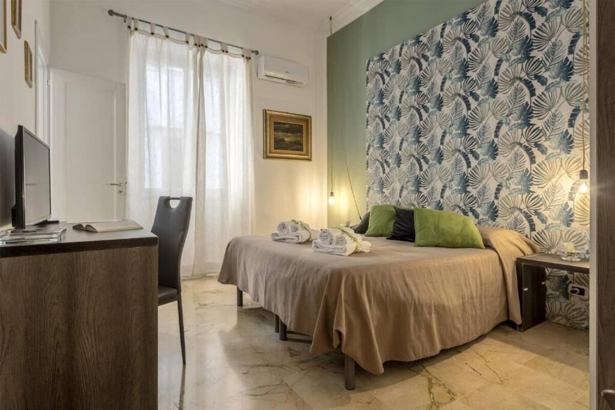 Habitació d'hotel amb un llit, escriptori, cadira, televisió i un mur amb un disseny decoratiu.