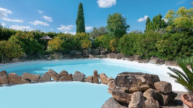 Une piscine bordée de rochers, entourée de verdure et d’arbres.