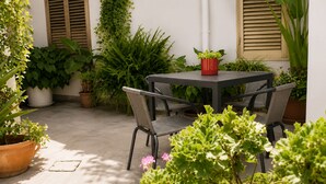 An outdoor patio area with a table and chairs, surrounded by potted plants and a white wall with shutters. - La Casa Più Bella | Near San Vito Lo Capo, Cornino & Monte Cofano (Custonaci)