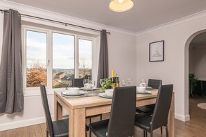 A dining area with a wooden table set for four, a view of the outdoors through large windows, and a framed picture on the wall.