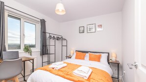 Habitación de hotel moderna con una cama grande, un escritorio con una computadora portátil, una ventana con cortinas y vistas al campo.