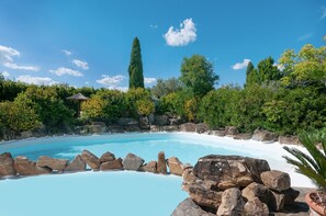Une piscine bordée de rochers, entourée de verdure et d’arbres.