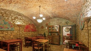 A rustic stone-walled room with wooden tables and chairs, a chandelier, and a cabinet with glassware. - Vin Santo – Independence and Relaxation with Private Garden (Reggello)