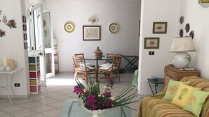 A living room with a glass coffee table, a sofa, a dining table with chairs, and a kitchen area in the background. - VILLA LA SCIROCCATA LEUCA (Santa Maria di Leuca)